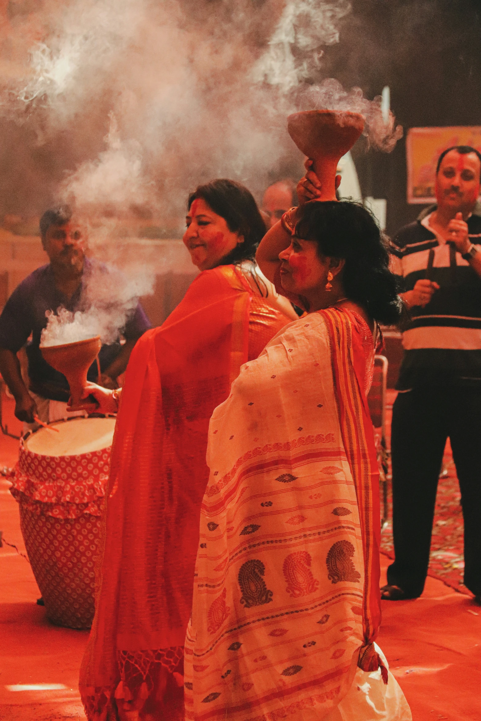 women and men standing around on red cloth with smoke coming from drums