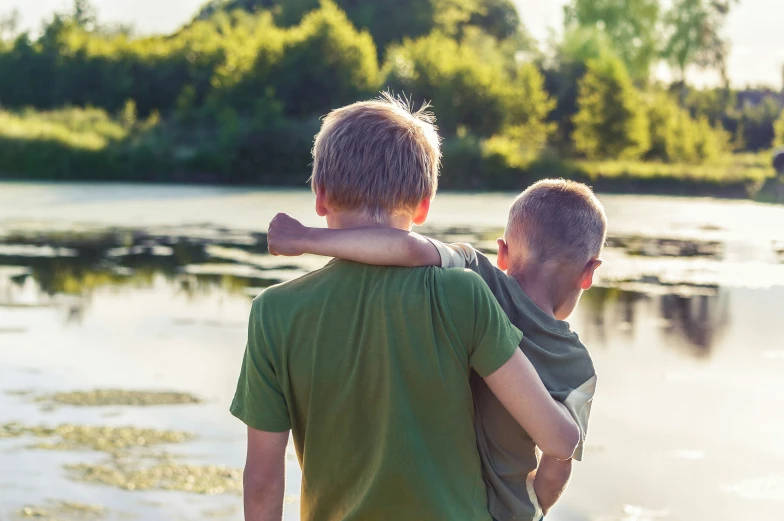 two boys hugging each other while standing by the water