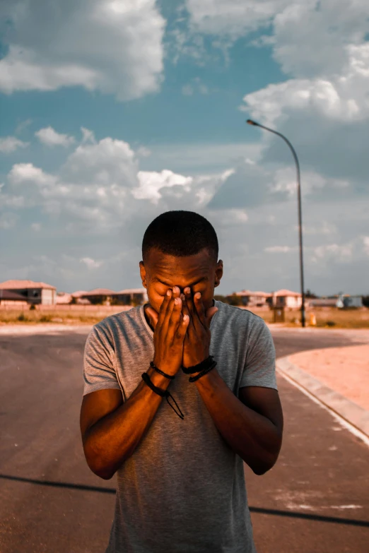 a young man standing in a deserted area covering his eyes