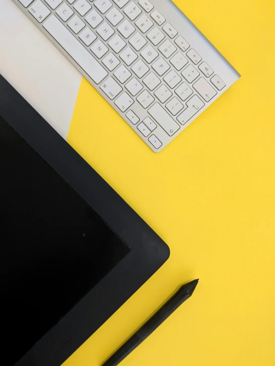 keyboard and tablet on a yellow desk with black pen