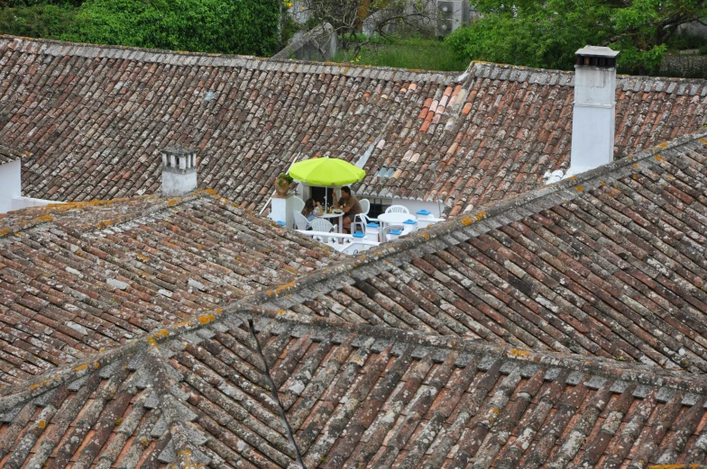 an aerial view of two people sitting on rooftops under a yellow umbrella