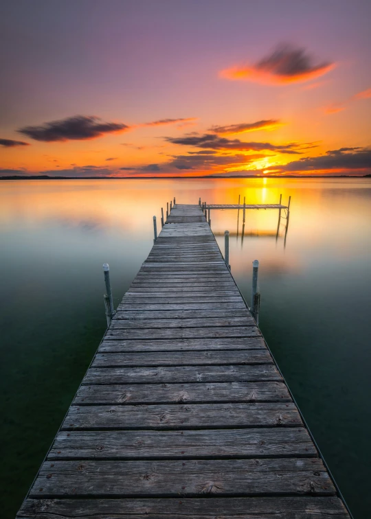 a boardwalk extends into the ocean towards a sunset