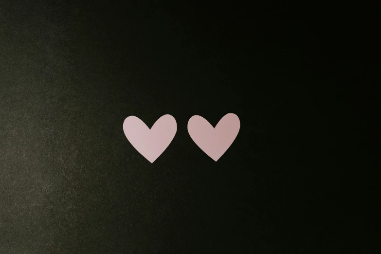 two hearts cut out of pink paper against a black background