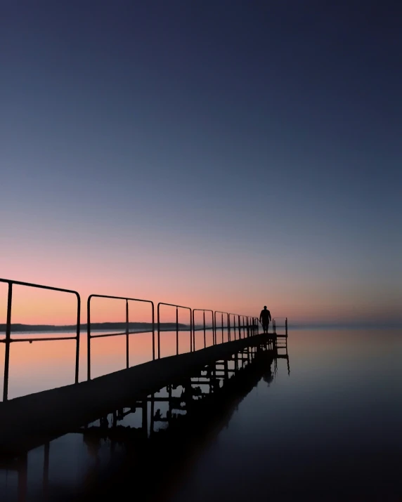 people standing on a long pier while the sun sets