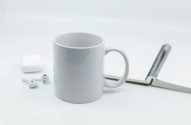 a white mug next to ear buds and a notebook