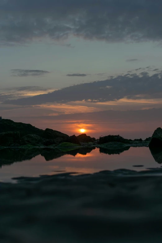 a body of water at sunset with the sun behind some rocks