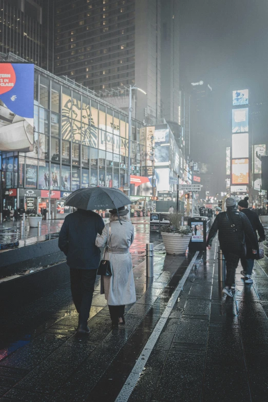 many people are standing on a city street at night, all holding umbrellas