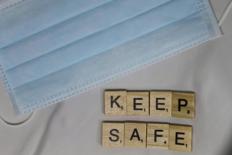 a face mask with blue face coverings and scrabble blocks spelling keep safe