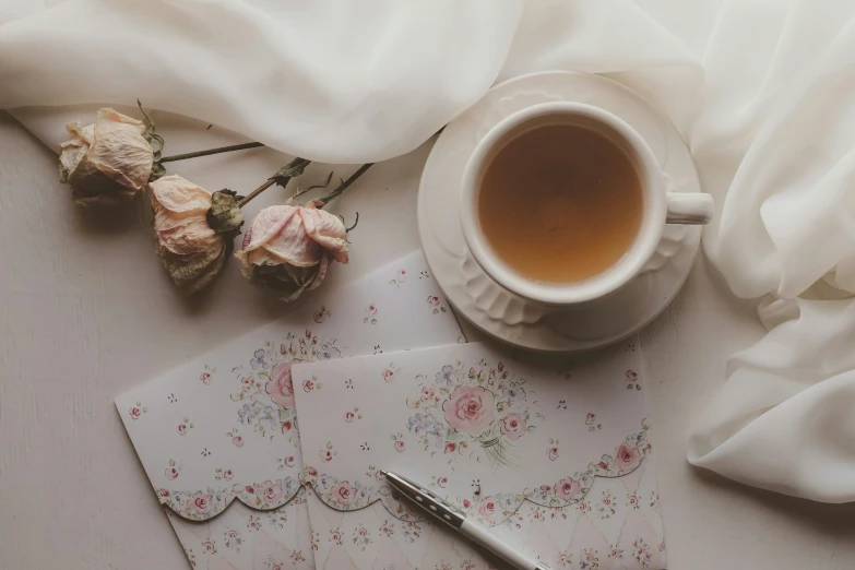 two roses and a cup of tea next to some papers