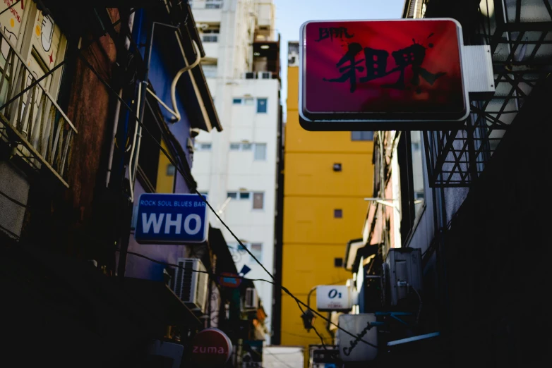 the side of a building in a city has a red sign and a blue sign that reads who?