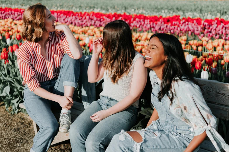 three women sit on a bench together in a field of flowers