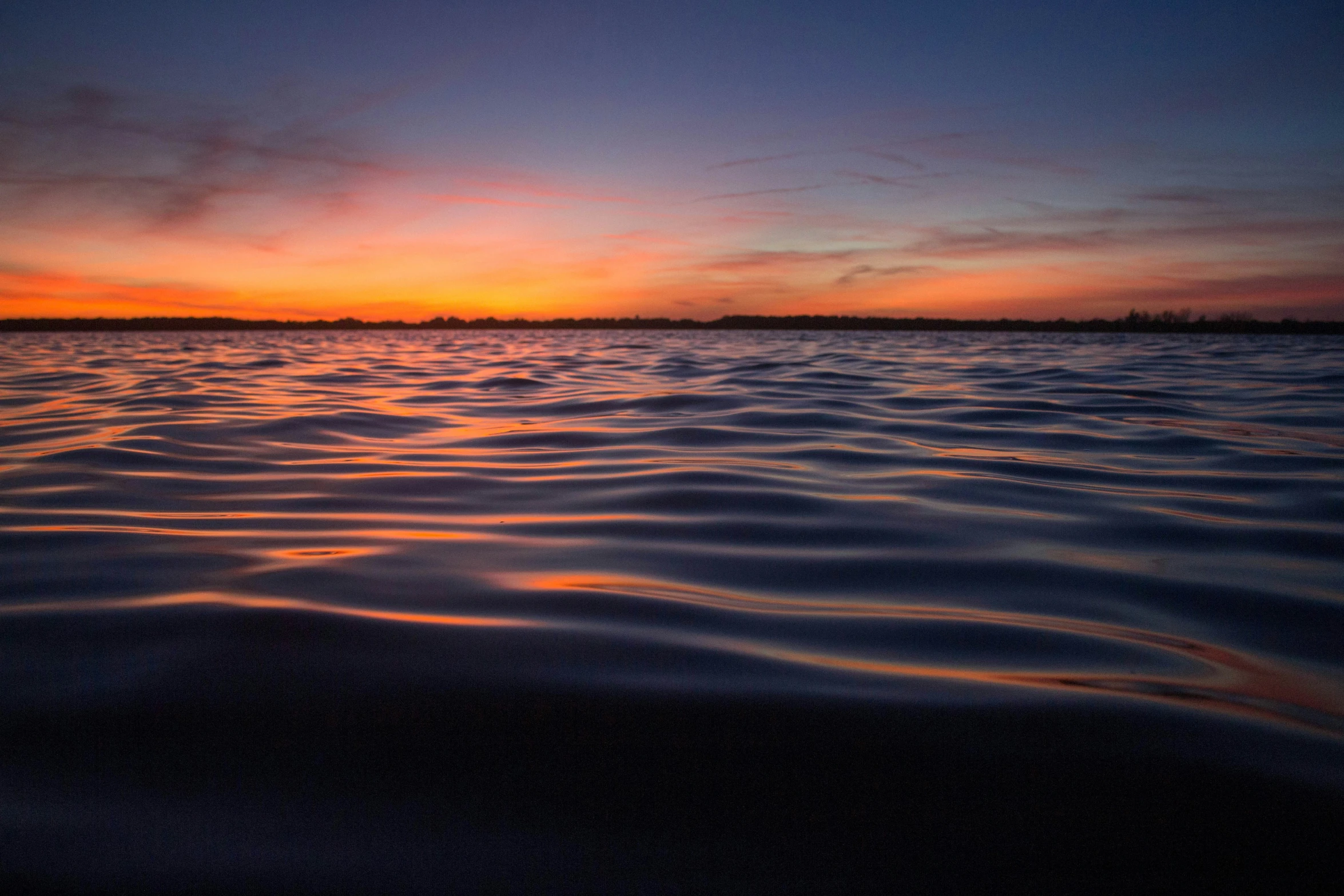 a sunset on a body of water, with a view of the horizon in the distance