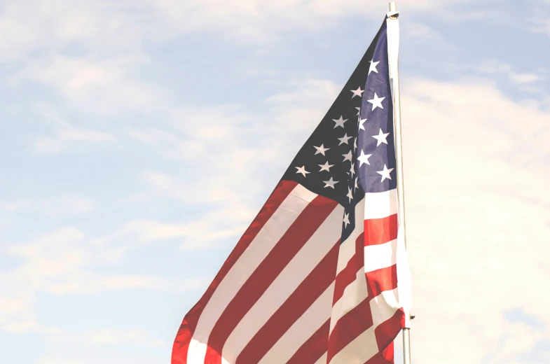 the american flag is flying in front of some white clouds