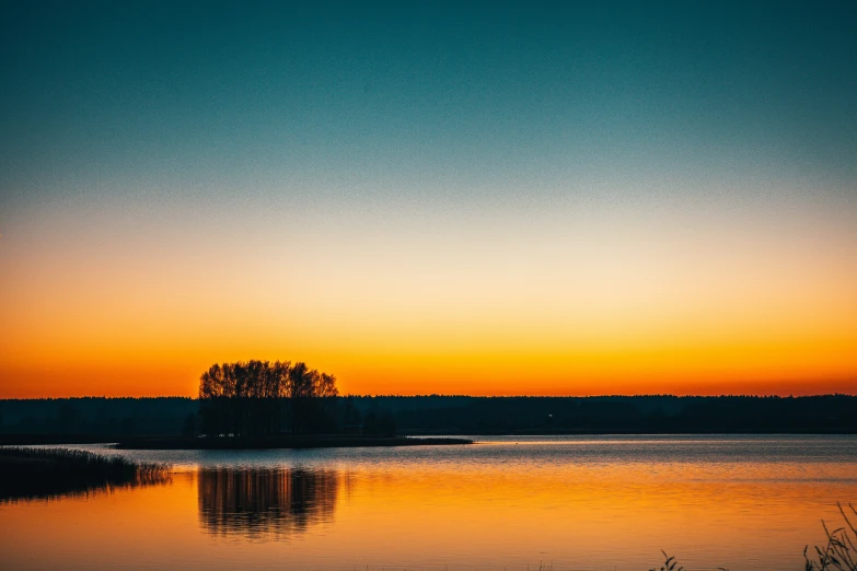 an orange and blue sky with trees in the background