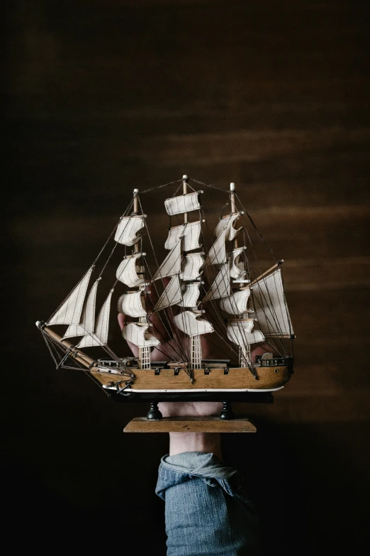 a man is holding his head up to a model of a pirate ship