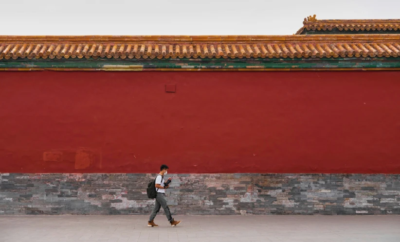 the man in the suit walks past a red wall