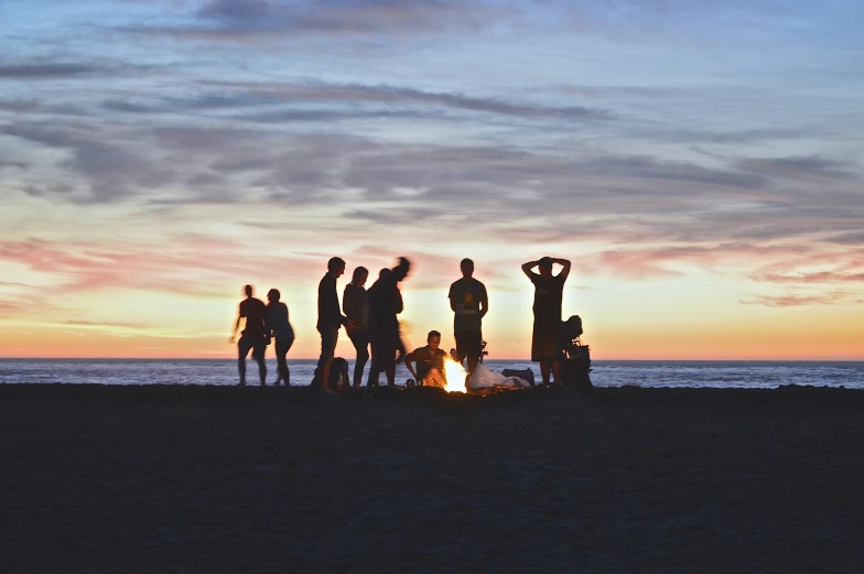 group of people near an open fire on the beach