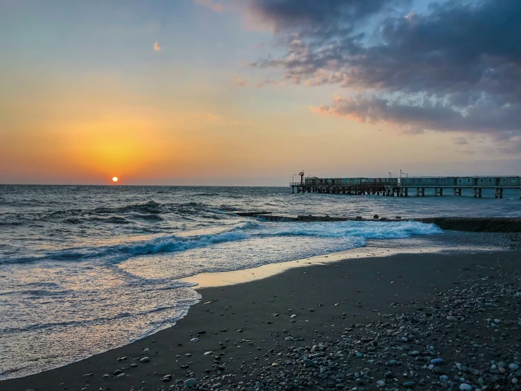 the sun sets over a sandy beach near a pier