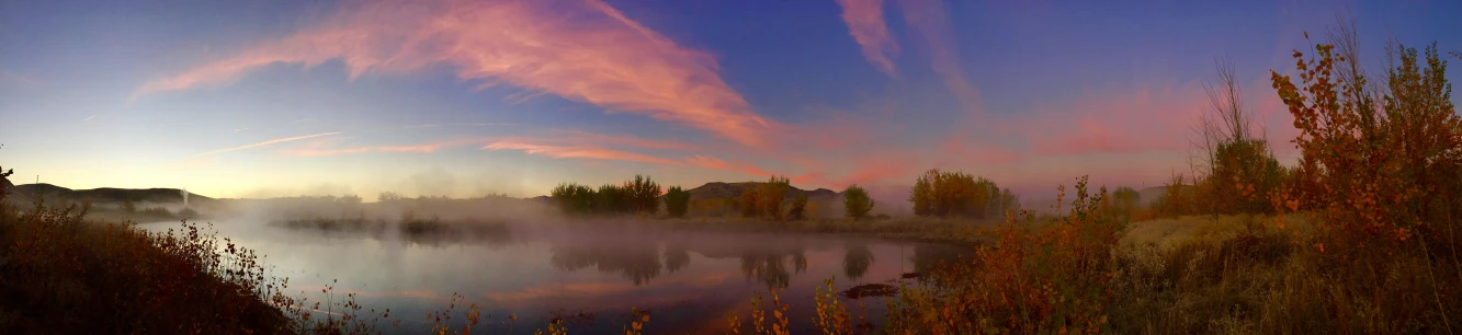 the sun is setting over a lake surrounded by woods