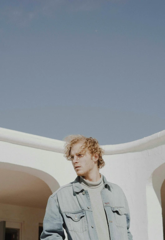 a person with curly hair, wearing a denim shirt and jeans