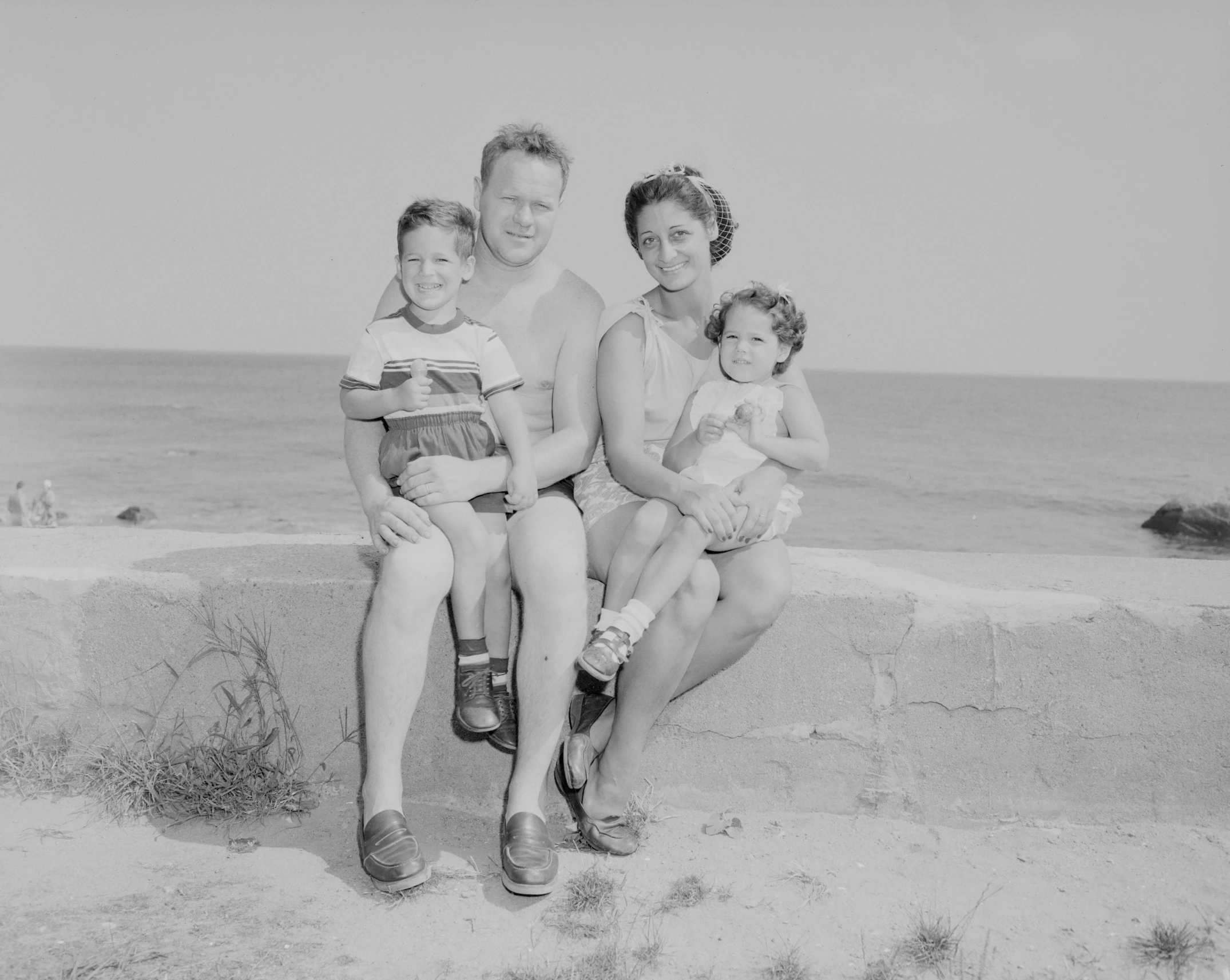 an old po shows a man and two children sitting on the wall near the ocean