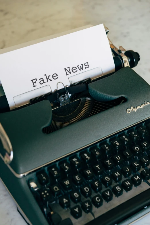 a typewriter with a fake news sign attached