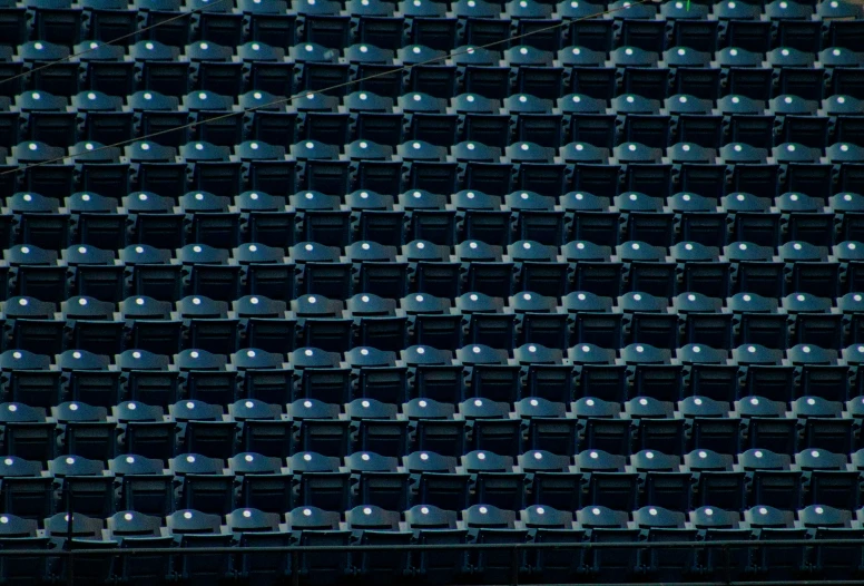 many rows of empty black chairs with one blue on at the end