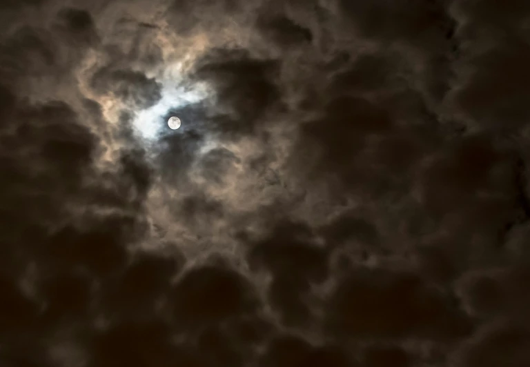 the moon shining through the clouds on a cloudy day