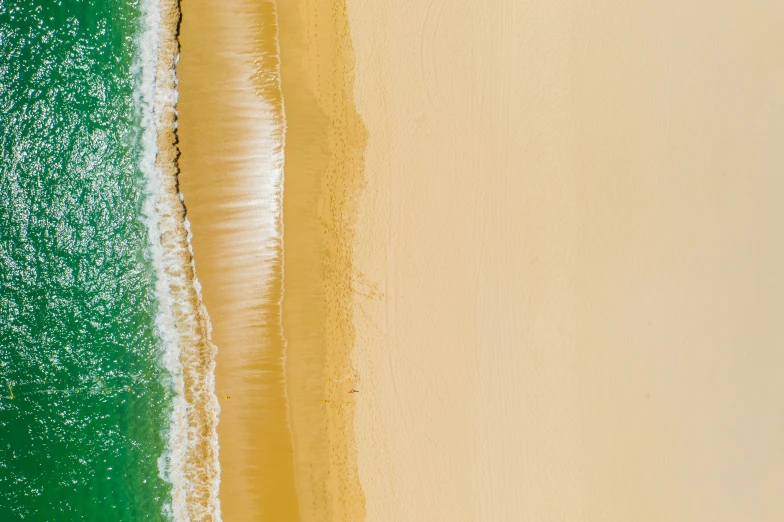 an overhead s of a sandy beach with waves and green water