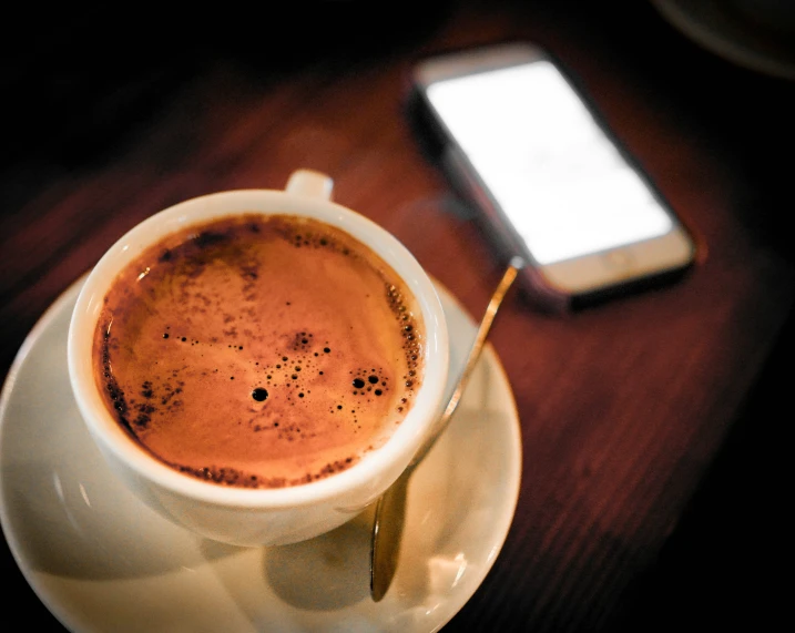 a cup of  chocolate on a plate next to a cellphone