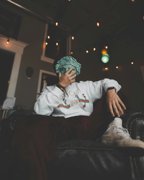 a male in a white shirt and a green head tie sitting on a couch