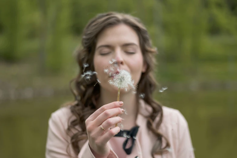 a girl blowing dandelion in front of her face