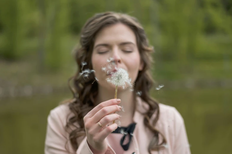 a girl blowing dandelion in front of her face
