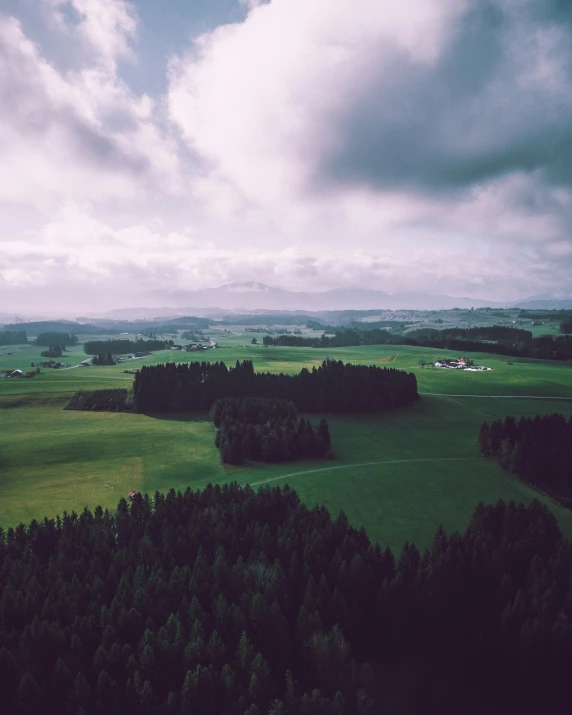 a cloudy sky over a large field with trees in it