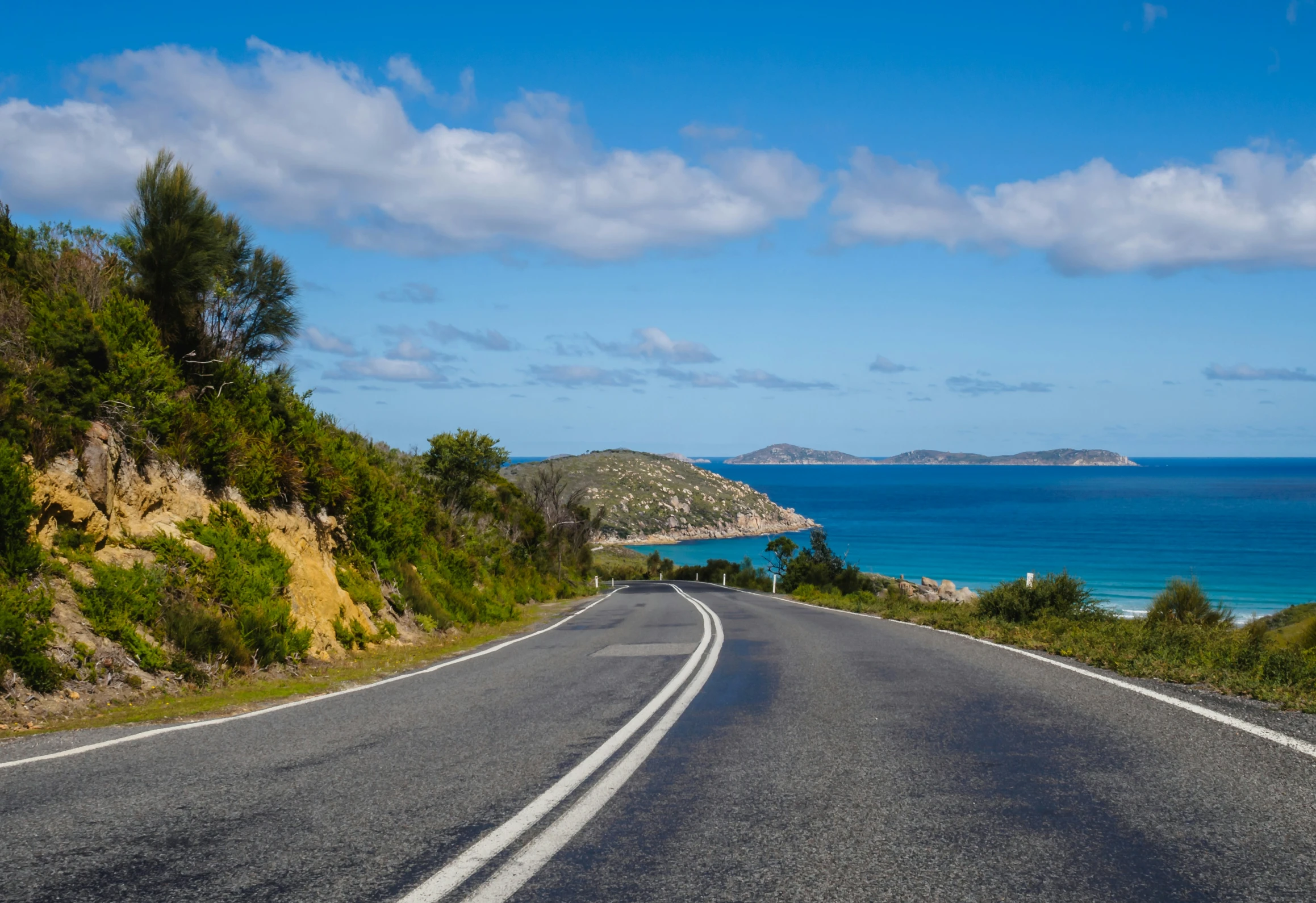 an empty road near the water is leading away