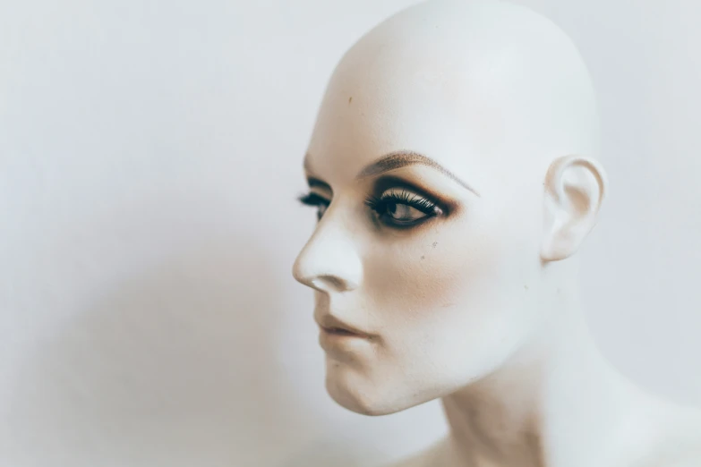 an adult mannequin head with a black and white makeup looks at soing while a hand holds the top