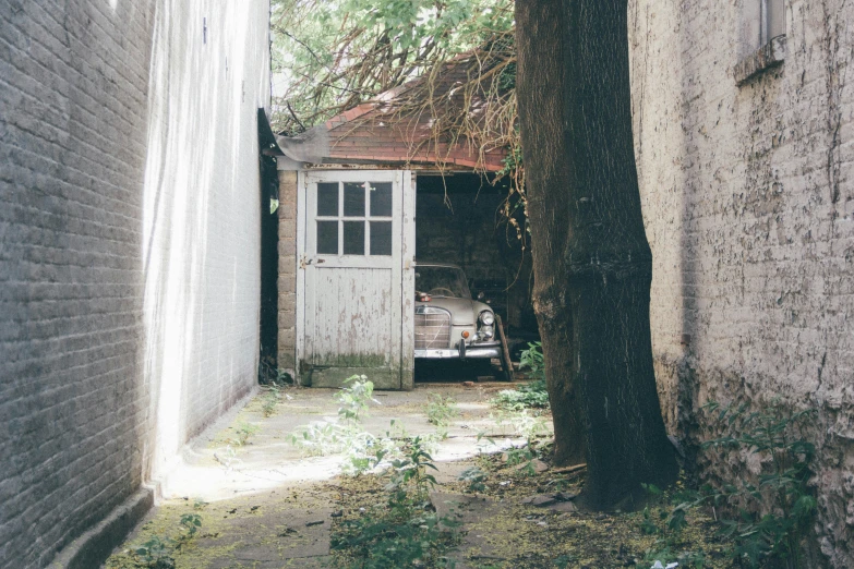 there is an old car in between a building and a tree