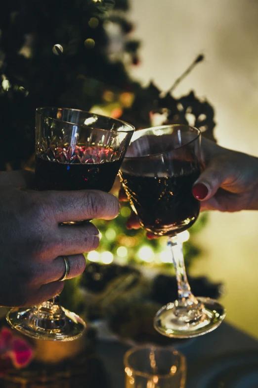 two people clinkling glasses next to a christmas tree