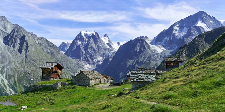 many buildings on a grassy hill in front of mountains