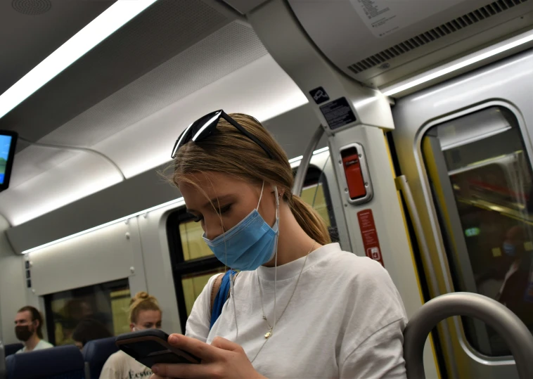 woman wearing a face mask and holding a smart phone while riding on a train