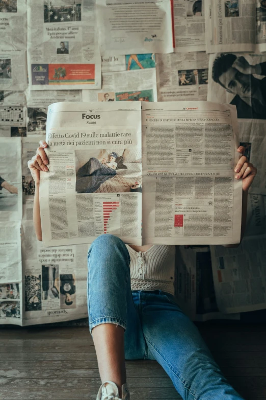 a woman reading a newspaper sitting in front of some newspapers