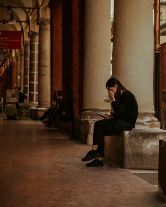 two people sitting on a bench next to pillars in a hallway