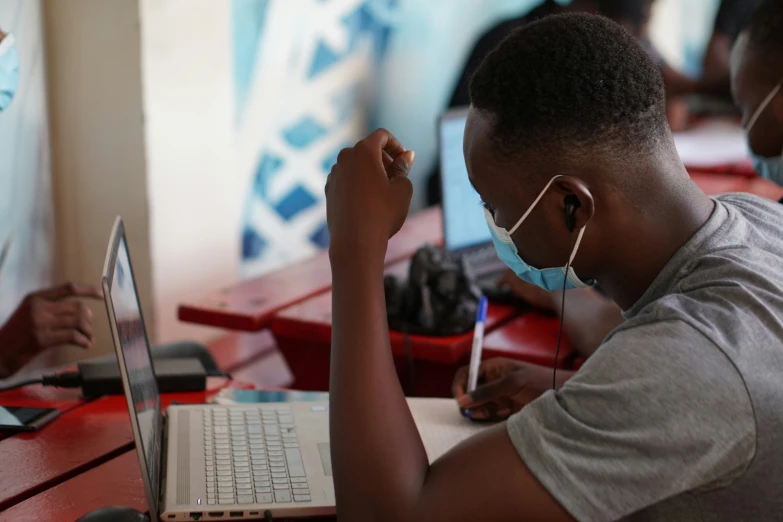 a person sitting with a mask on, typing on his laptop