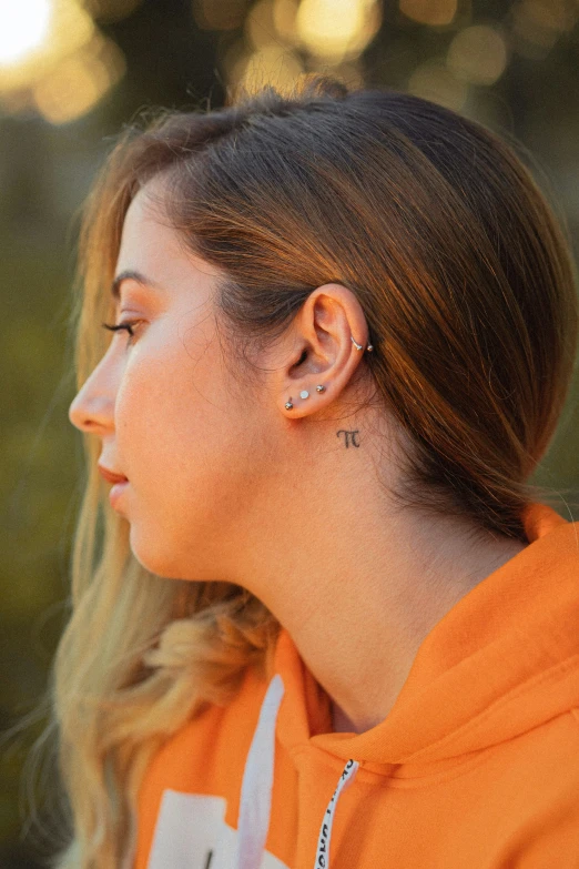 a woman in an orange sweatshirt wearing a pair of ear posts