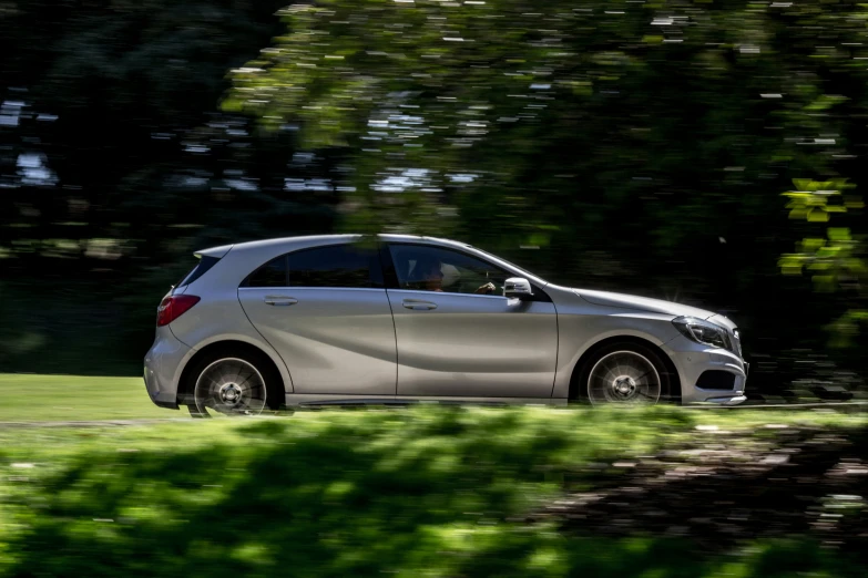 a grey car driving on the road in front of trees