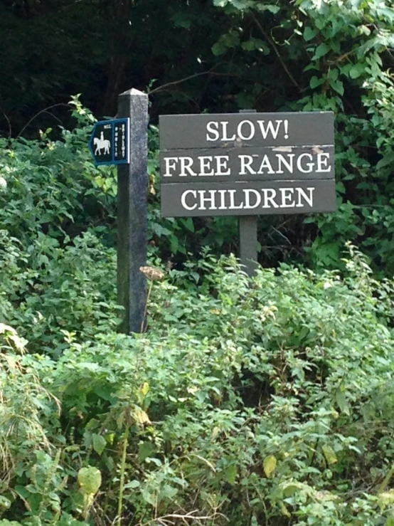 a sign reading slow free range children next to some bushes