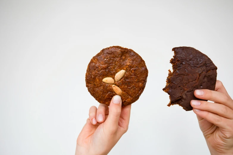 two hands holding cookies made of brownie and almond