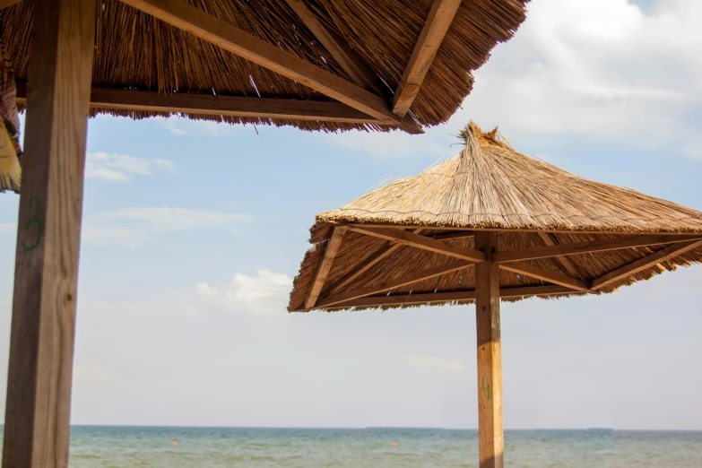 an umbrella sitting under two straw huts by the ocean