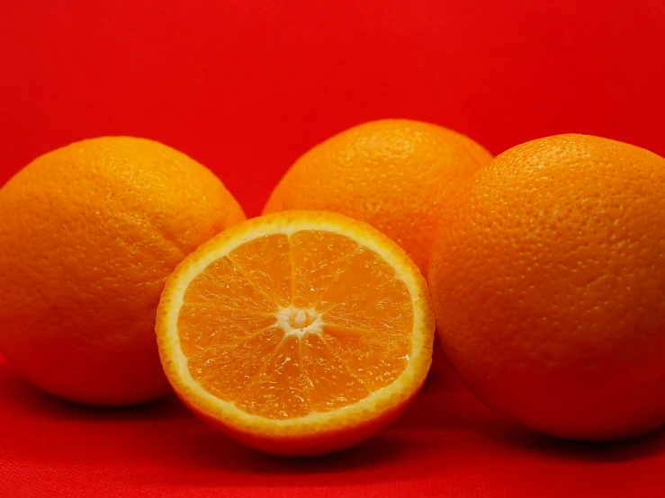 three halves and one whole orange sit on a bright red background