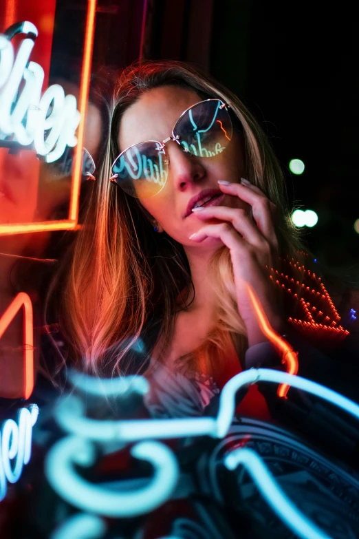 a woman sitting next to neon lights holding a cell phone